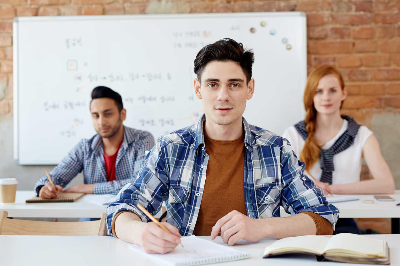 Jovens posam sentados em suas mesas durante aula