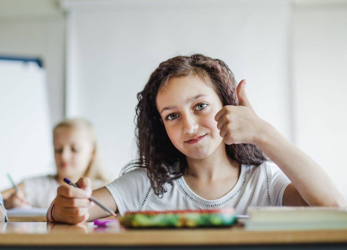 Menina posa para foto sentada em sua mesa durante a aula 