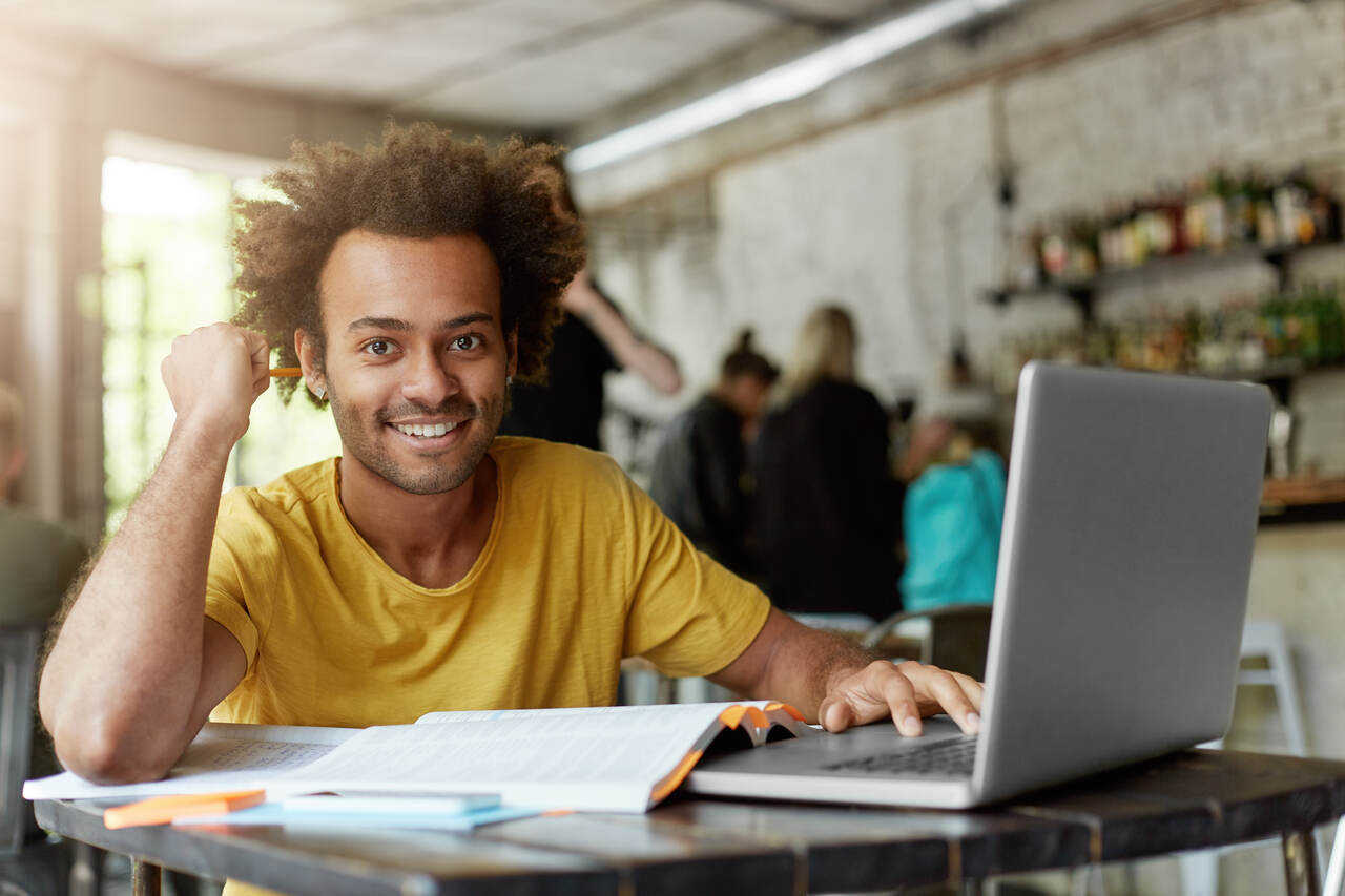 Jovem posa sorrindo enquanto estuda em seu notebook